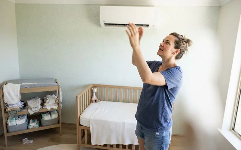 A wall-mounted split system positioned to one side of a nursery, away from direct airflow over a cot